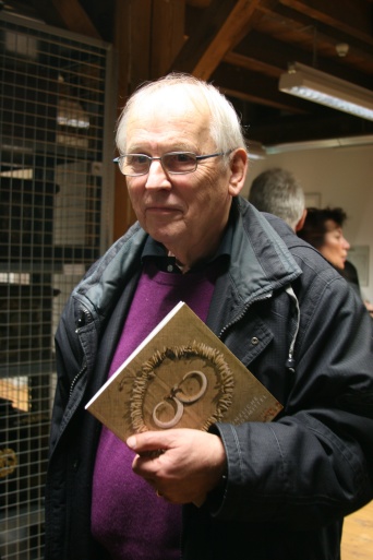 Ein Herr mit lila Pullover trägt stolz ein Buch in seiner Hand