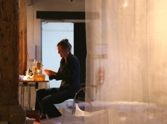 Eine Dame näht an einer beleuchteten Nähmaschine. Rechts im Bild ist ein transparenter Stoff zu sehen.