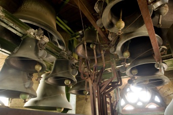 Zehn Glocken im Verbund von unten aufgenommen. Rechts im Bild der Blick ins lichtdurchströmte Turmfenster.