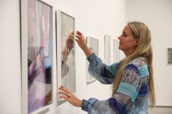 Eine Frau mit blondem langen Haar hängt Ausstellungsbilder.