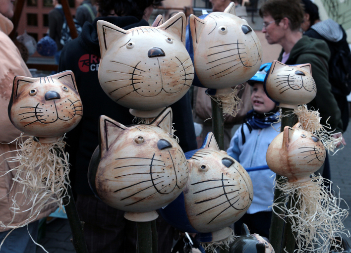 Sieben in Ton gearbeitete Katzenköpfe. Dahinter Besucher des Erfurter Töpfermarktes