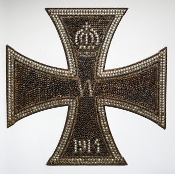 Kreuz mit zahlreich eingeschlagenen Nägeln, oben in Form einer Krone.