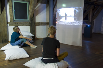 Foto: Die Sage vom gewünschten Kind: Videopräsentation in der Ausstellung "Bodenschätze" © Stadtverwaltung Erfurt / D. Urban Zwei Frauen sitzen vor einer Videowand.