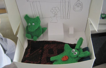 zwei grüne Plüschtiere in einer gestalteten Papp-Kiste