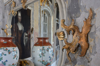 Links eine Vase, die sich im muschelwerkgeschmückten Spiegel wiederfindet.