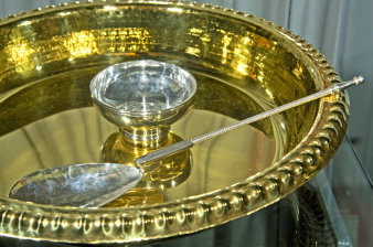 Löffel und kleine Silberschale in einer größeren, goldfarbenen Schale mit Zierrand.