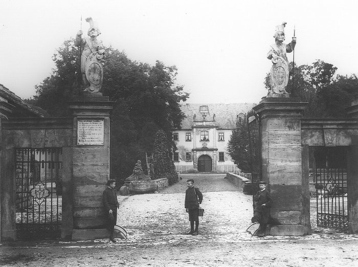 Ehrenhof am Schloss Molsdorf. Aufnahme aus dem Jahre 1920. Das Schild trägt folgende Aufschrift: "Mit alleiniger Ausnahme der Bewohner des Schlosses und der Gutsgebäude, sowie des Gesindes und der Tagelöhner des Guts, wird hiermit untersagt über den Gutshof zu gehen. Zuwiderhandelnde trifft die gesetzliche Strafe. Gotha den 26. Sept. 1883, herzogl. Domänenkasseverwaltung" Drei Jungen mit Knickerbockern stehen am Steinportal des Schlosseinganges.