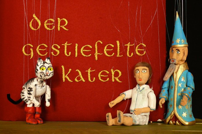 Henning Hacke, Märchen für Kinder "Der gestiefelte Kater" Drei Marionetten vor einem roten Hintergrund.