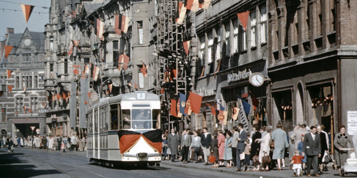Eine mit zahlreichen DDR-, FDJ- und Arbeiterfahnen geschmückte Häuserzeile. Im Vordergrund eine mit einer Fahne geschmückte Straßenbahn.