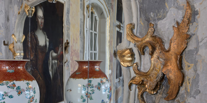 Links eine Vase, die sich im muschelwerkgeschmückten Spiegel wiederfindet. 