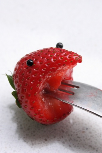 Eine gestaltete Frucht mit aufgesetzten Augen und einer Gabel im "Erbeermund".
