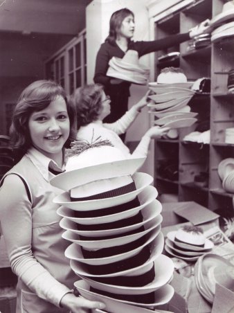 Junge Frau hält einen Stapel mit Faschingshüten, im Hintergrund Regal mit Faschingsartikeln