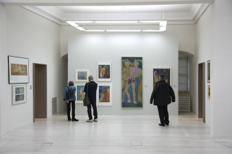 Drei Besucher betrachten die an der Wand hängenden Bilder