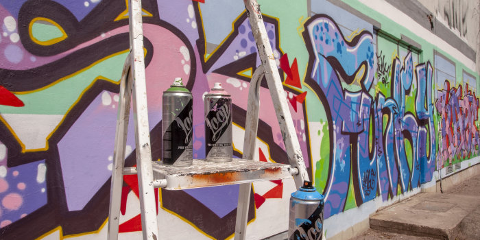 Wand mit Graffiti, davor eine Leiter mit Spraydosen