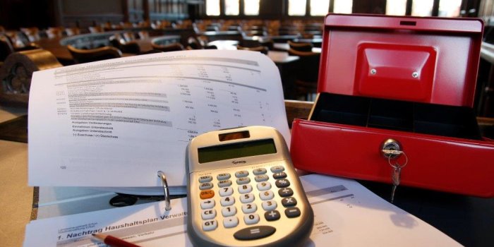 Ein Taschenrechner, eine offene Kasse und ein Papierstapel liegen auf dem Pult im Ratsitzungssaal