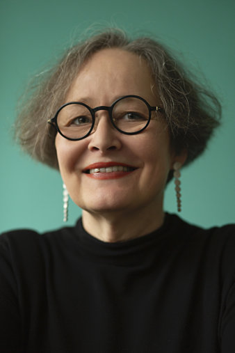 Porträt einer Frau, die Schmuck und eine Brille trägt.