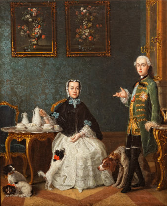 Eine junge Dame, am Tisch sitzend und die Kaffeekanne haltend, der junge Mann, stehend, die Hand auf einem Konsolentisch abstützend. Beide in zeitgenössischen Gewändern. Im Hintergrund seidenbespannte Wände und zwei Blumenstillleben. Im Vordergund drei Hunde.