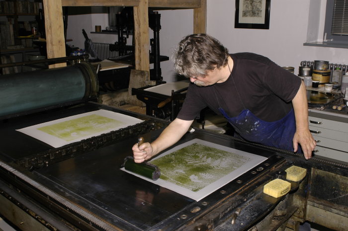 Ernst August Zimmermann in der Grafik-Werkstatt im Benary-Speicher Ein Mann, rechts im Bild, führt eine Rolle über eine Grafik.