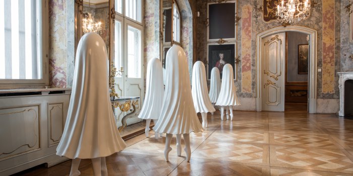 Sechs tanzende Röcke in einem Barocksaal.