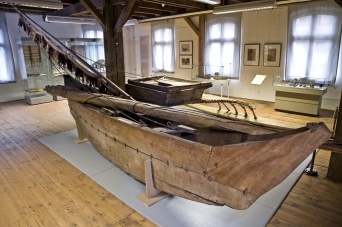 Foto: Auslegerboot im Schaudepot des Benary-Speichers © Stadtverwaltung Erfurt / D. Urban Ein Boot aus Holz, im Hintergrund hohe und flache Vitrinen. Alles auf einem Holzfußboden.