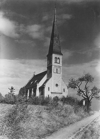 Foto: Gustav-Adolf-Kirche Melchendorf, 1954 © Stadtverwaltung Erfurt / Stadtarchiv Kleine Kirche mit hohem Turm, davor ein Feldweg und ein einzelner Baum.