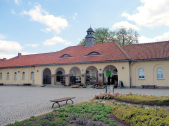 Foto: Blumenladen am Haupteingang, alte Feierhalle © Stadtverwaltung Erfurt Alte Feierhalle mit Blumenladen. Dreiteiliges eingeschossiges Gebäude mit Ziegeldach. In der Mitte befindet sich hinter 5 Bogenöffnungen der Blumenladen. Vor dem Gebäude befindet sich eine gepflasterte Platzfläche, die von Staudenflächen eingefaasst ist.