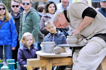 Foto: Töpfermarkt © Barbara Naumann Ein Töpfer fertigt an seiner Töpferscheibe ein Gefäß, Zuschauer sehen dabei zu.