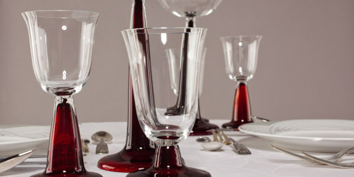 Fünf filigrane Gläser auf weißem Tischtuch, zwei Teller und verschiedene Besteckteile