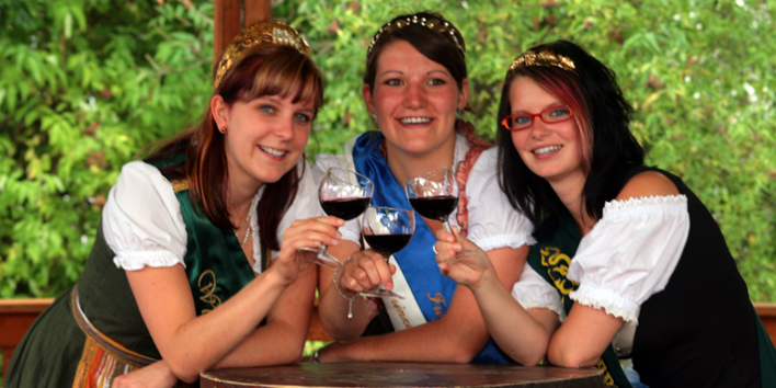 Drei junge Weinköniginnen mit Rotweinglas in der Hand.