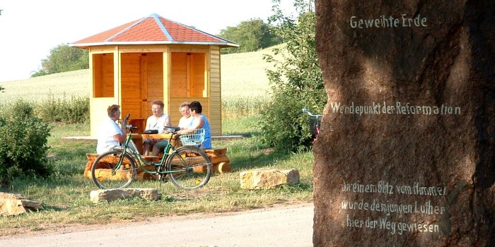 Lutherstein in Stotternheim Ein Gedenkstein rechts, eine Wandergruppe links am Tisch. Im Hintergrund ein Pavillon.