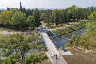 Luftaufnahme einer Brücke, die über einen Fluss in einen Park mit vielen Bäumen führt