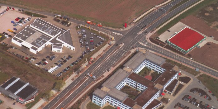 Luftaufnahme einer mehrspurigen Straße im Kreuzungsbereich mit Gewerbeflächen und Gebäuden