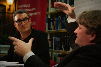 Carsten Rose und Prof. Dr. Dr. Helge Peukert sitzen an einem Tisch und unterhalten sich.