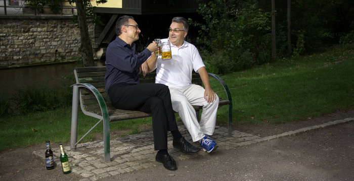 Zwei Männer sitzen Bier trinkend auf einer Bank.