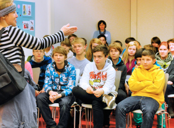 Lesung in der Kinder- und Jugendbibliothek Eine Gruppe Jugendlicher hört einer Autorin zu.