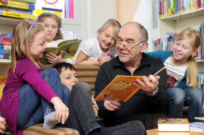 Im Leseraum der Bibliothek Drosselberg Ein Mann liest Kindern aus einem Buch vor.