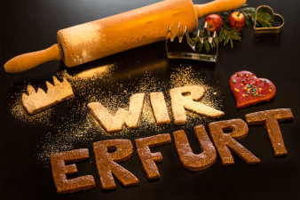 Selbst gebackene Plätzchen auf Küchentisch. Sie bilden einen Schriftzug "Wir lieben Erfurt". Ausstechförmchen, Mehl und Nudelholz befinden sich im Bildhintergrund.  