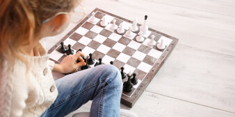 Mädchen sitzt auf dem Fußboden. Vor ihr liegt ein Schachbrett, auf dem Schachfiguren stehen.