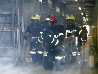 3 Feuerwehrmänner mit Ausrüstung und Atemschutz kniehend in verrauchtem Raum