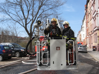 Das Foto zeigt zwei Feuerwehrleute im Korb einer Feuerwehrdrehleiter nach einem Einsatz zur Brandbekämpfung.