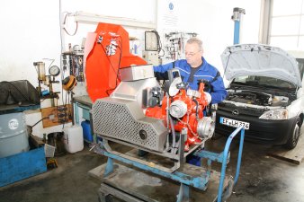 Mann in blauer Kleidung hinter einem technischen roten Gerät auf Bock in einer Werkstatt