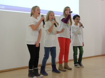 Das Foto zeigt einen Rap-Gesang von 4 Grundschülern, welcher sich dem Thema Umwelt widmet.