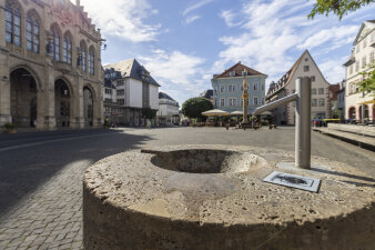 steinerner Trinkbrunnen auf einem Platz, im Hintergrund Altstadt-Kulisse