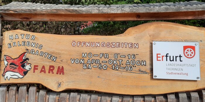 ein Stück Holz trägt den Titel und die Öffnungszeiten des Naturerlebnisgartens Fuchsfarm