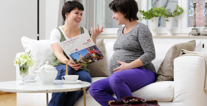 Hebamme und schwangere Frau sitzen auf einer Couch