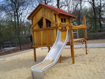 große Sandfläche mit Spielhaus aus Holz mit rotem Dach und Rutsche