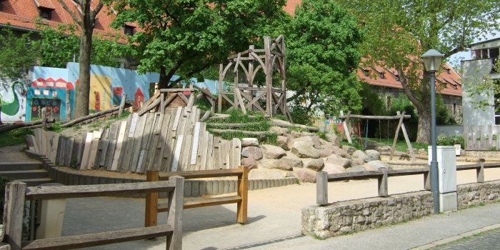 Foto: Spielplatz Glockengasse: Rutschenturm und Doppelschaukel © Stadtverwaltung Erfurt großer Hügel aus Steinen, Holz und Rasen mit Rutschenturm aus Holz und Schaukel mit zwei Sitzen