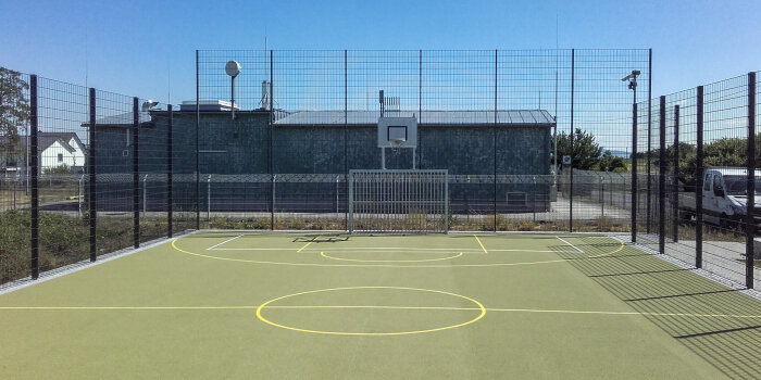 eingezäuntes Sportfeld mit Basketballkorb und Fußballtor