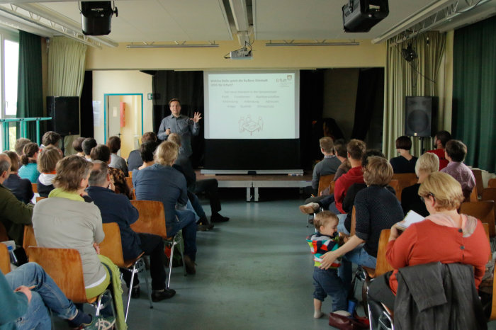 Erste Bürgerwerkstatt zur Entwicklung der Äußeren Oststadt Bürgerdialog in einer voll besetzten Schul-Aula; ein Mitarbeiter der Stadtverwaltung erläutert den Bürgern die Planungen an einer Tafel.