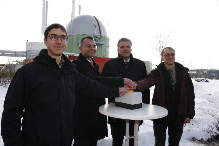 Manager der Stadtwerke und der Oberbürgermeister beim synbolischen Knopfdruck am Stehtisch, im Hintergrund ist die Anlage mit der Kuppel des Gärbehälters zu sehen.